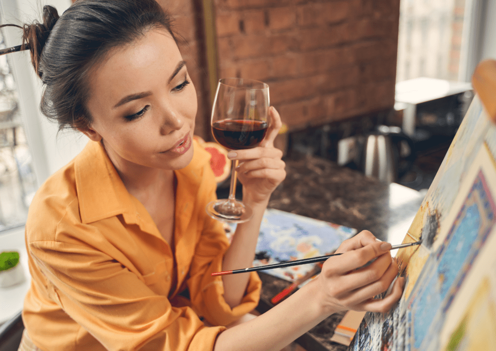 Woman holding wine glass while painting on a canvas