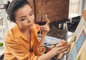 Woman holding wine glass while painting on a canvas